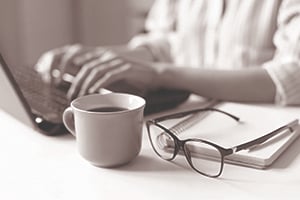 person working on laptop computer with glasses and coffee next to them