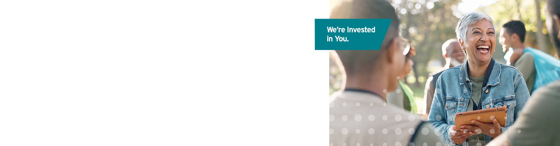 Teal label reads “We’re invested in you,”  with a smiling older woman holding a tablet while speaking with people outdoors
