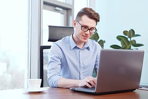 Young man with glasses typing on a laptop