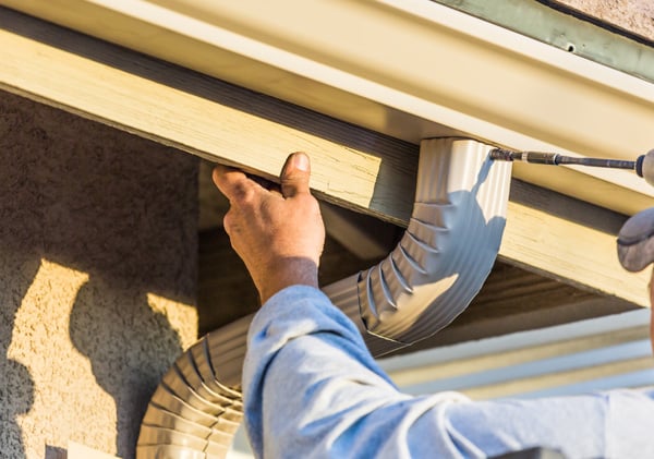 Worker Attaching Aluminum Rain Gutter and Down Spout to Fascia of House