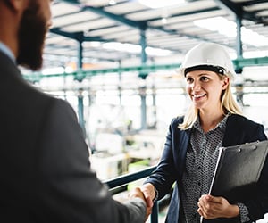 smiling man and woman shaking hands in manufacturing warehouse