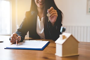 smiling woman handing over keys with paperwork