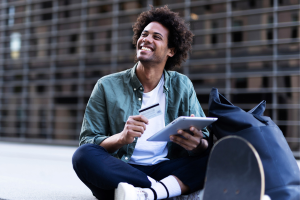 Male student holding debit card and tablet computer smiling