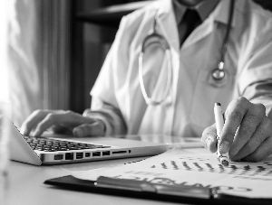 doctor working on a laptop and writing