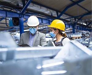 Man and woman with hard hats and masks working in a manufacturing plant