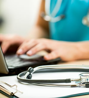 doctor working on a laptop with a stethoscope next to her