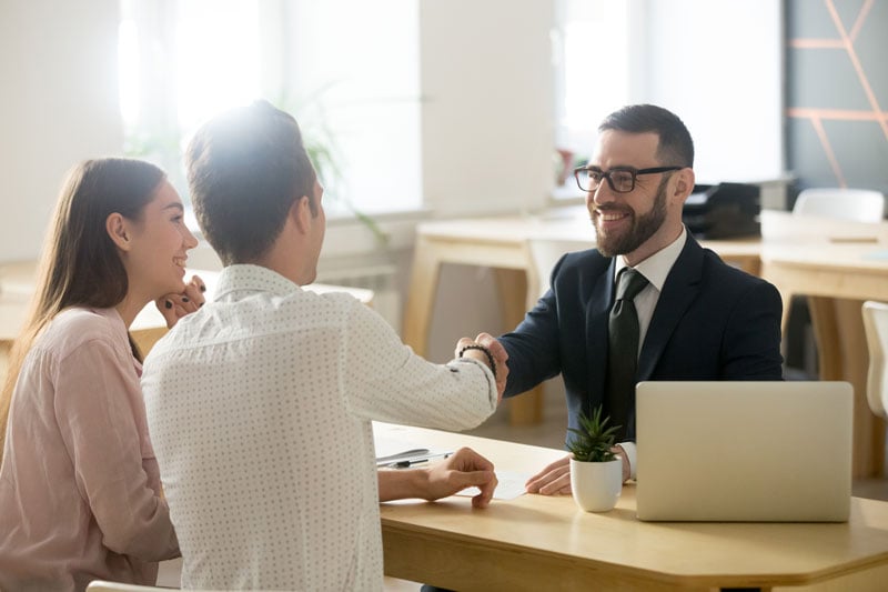 A young man and woman shake hands with a loan expert in his office.